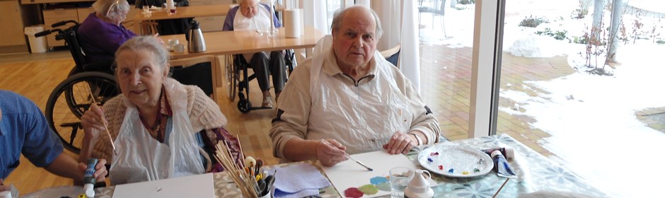 To ældre mennesker sidder og maler billeder i et daghjem