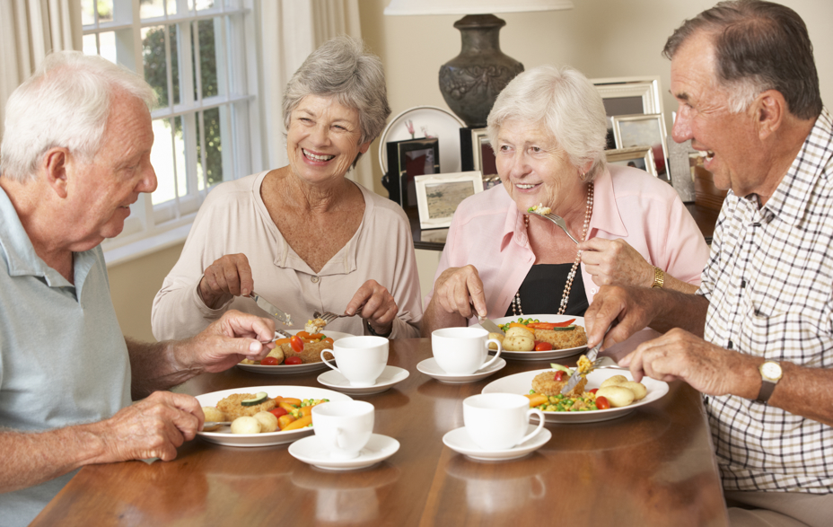 4 ældre mennesker sidder ved bord og spiser middag