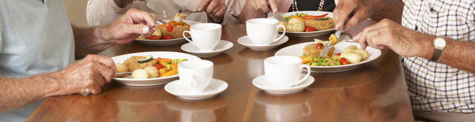4 ældre mennesker sidder ved bord og spiser middag