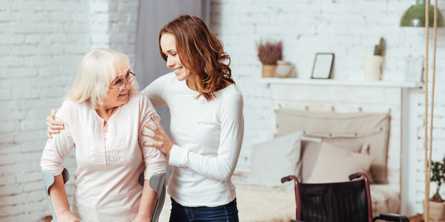 Billedet viser en yngre kvinde, der hjælper en ældre kvinde med krykker.