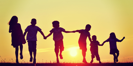 6 børn der løber hånd i hånd i solnedgang