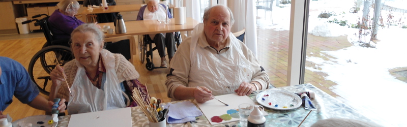 To ældre mennesker sidder og maler billeder i et daghjem